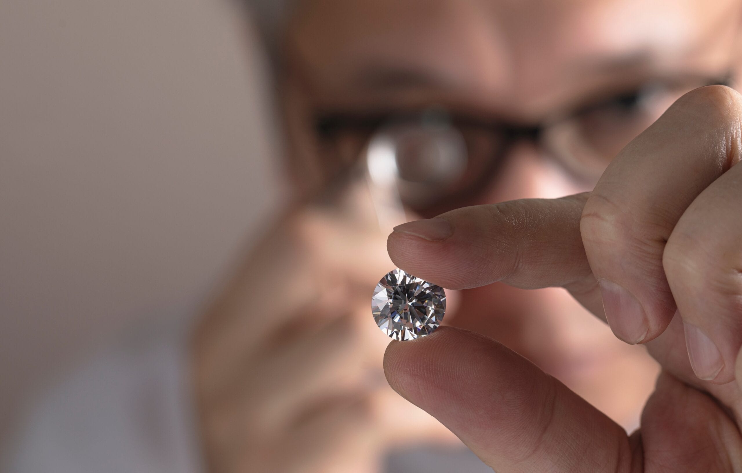 Un expert examine à la loupe un diamant taille brillant tenu entre deux doigts