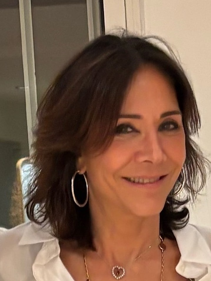 Portrait de Véronique Devinaz, dirigeante de « La Cote des Bijoux », en chemise blanche, portant un sautoir orné de pierres de couleur et un pendentif serti